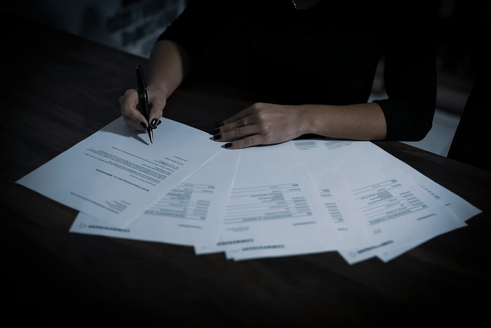 Des documents étalés sur une table, une main tient un stylo